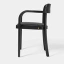 A modern black dining chair with a curved armrest, black upholstered seat, and a small gold accent on the front apron, shown against a plain light gray studio background.