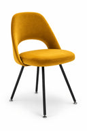 A modern accent chair with a curved mustard yellow velvet upholstered seat and backrest, supported by four slim black metal legs with silver ball feet, set against a plain white studio background.