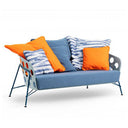 A blue upholstered outdoor loveseat with a perforated metal frame and blue legs, styled with several throw pillows including two bright orange pillows and two blue-and-white striped pillows, on a white background.