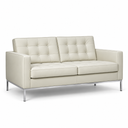 A modern two-seater sofa upholstered in cream-colored leather with tufted back cushions and slim silver metal legs, shown against a plain white background.