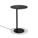 A minimalist black metal side table with a round top, a single central pedestal leg, and a circular base, shown on a light gray background with its power cord visible.