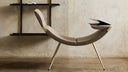 Clop by Luxy in taupe upholstery against architectural concrete wall, side view showing curved seating and tapered legs