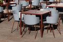Red Midj Fold square metal outdoor café tables surrounded by light gray armchairs on a paved terrace