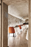 Midj Lea S M CU dining chairs with orange leather upholstery and slim metal legs in a vaulted restaurant