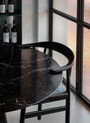 Detail view of Midj Oslo P L TS ashwood dining armchair with upholstered seat beside a dark marble table and window