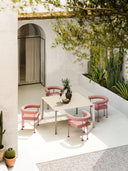 Four pink Qua-ndo P M TS Armchairs by Midj with thin metal legs surround a light beige outdoor table