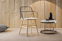 Midj Strike P L armchair showing black steel wire back, curved armrests and natural wood legs beside a round side table