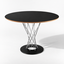 A round dining table with a black top, a light natural wood edge, and a chrome wire crisscross pedestal base on a black circular foot, shown on a white studio background.